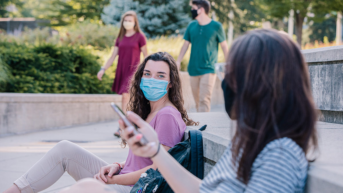Students sitting outdoors and wearing paper masks over their mouth