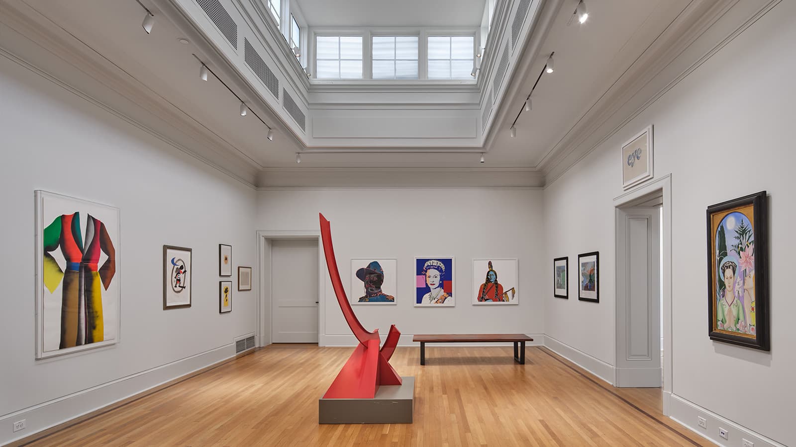 A high ceiling, well-lit gallery room with frames on the wall and red sculpture in the center of the room