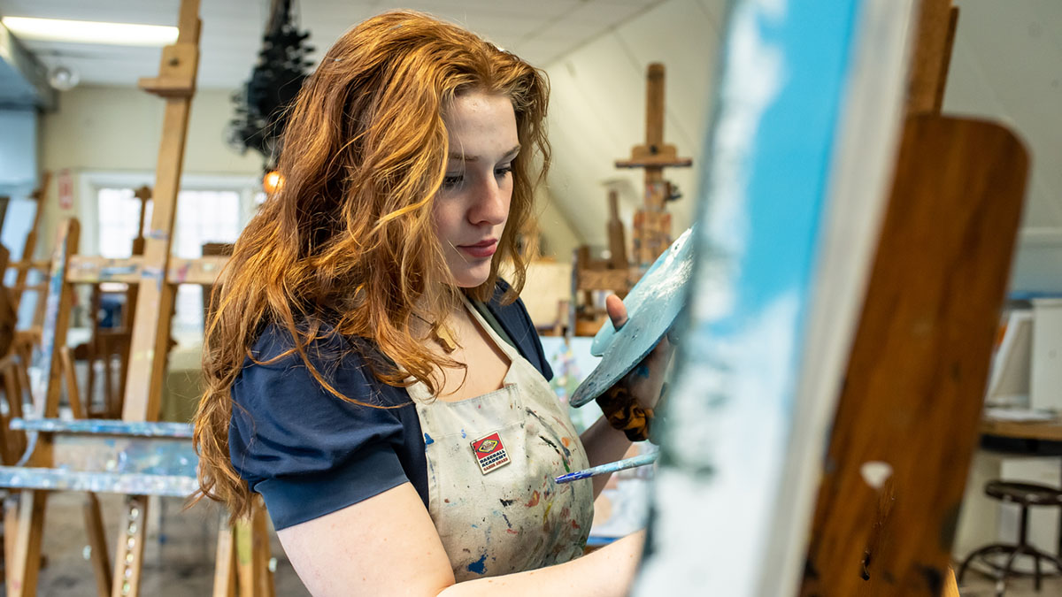 A woman standing at an art easel painting on a canvas