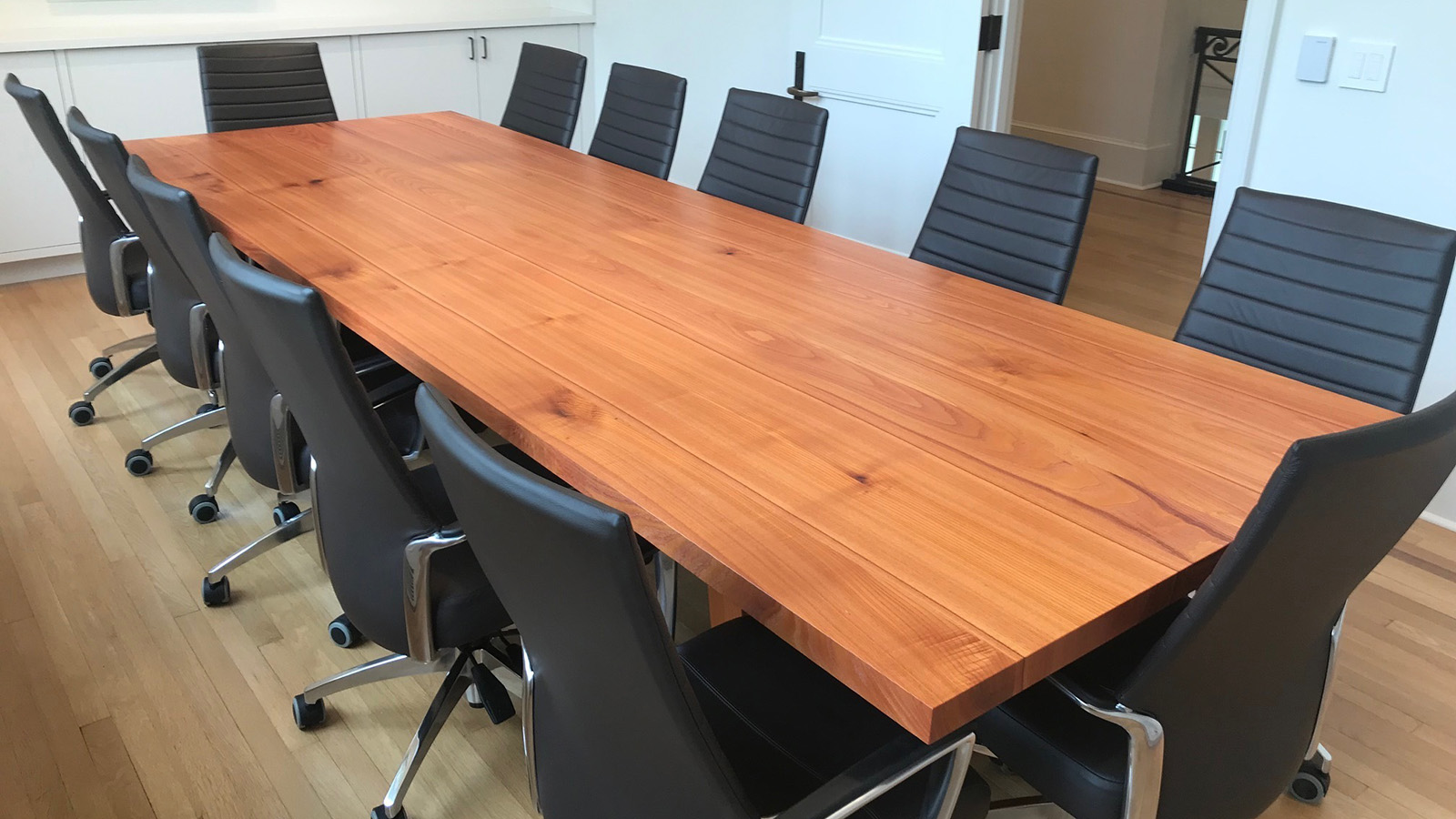 Long wooden conference room table surrounded by black chairs in an office